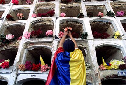 Un hombre cubierto con una bandera colombiana deja unas flores en los nichos donde se ha enterrado a varias víctimas del atentado.