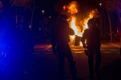 Mossos d´Escuadra officers watch as a garbage container set on fire by protesters burns.