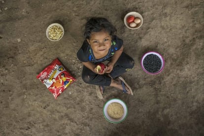 Solo uno de cada tres niños recibe una alimentación lo suficientemente variada como para poder crecer adecuadamente. En la imagen, Jessica Domingo, guatemalteca de cinco años, come una manzana y posa en el suelo del patio de su casa. En los platos hay frijoles, maíz, arroz, tomates, huevos e Incaparina (una mezcla de harina de maíz y harina de soja fortificada con vitaminas y minerales que se usa como complemento alimenticio). Estos alimentos son los que su madre, Catalina Ramírez, suele incluir en su dieta.