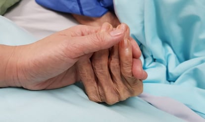 Una mujer coge la mano de una anciana en un hospital.