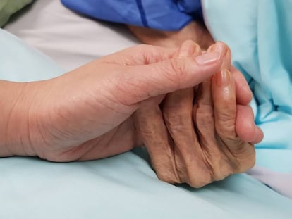 Una mujer coge la mano de una anciana en un hospital.