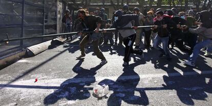 Manifestantes intentan derribar una barrera policial que protege el Parlamento con la ayuda de un poste.