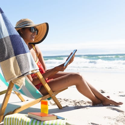 Un chica sentada en la playa en una silla plegable.