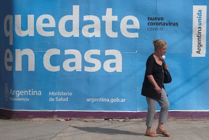 Uma mulher passa em frente a um cartaz governamental que pede à população que fique em casa.