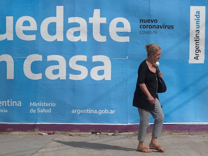 Uma mulher passa em frente a um cartaz governamental que pede à população que fique em casa.