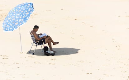 Un hombre lee bajo su sombrilla en la orilla de la playa de La Concha de San Sebastián este jueves.