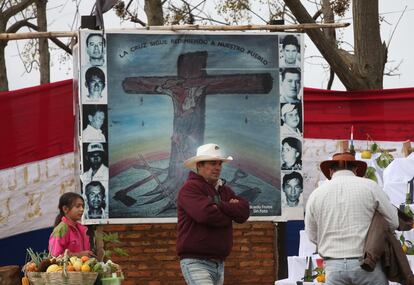 Varios vecinos pasan por delante de un poster con una cruz cristiana en el acto de conmemoración del 2º aniversario de la matanza de seis policías y once campesinos en tierras de Marina Kue, en Curuguaty, Paraguay.