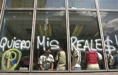 Un grupo de personas espera en un banco de Caracas, tras una pintada que exige poder retirar el dinero.