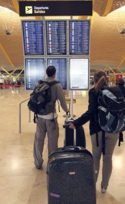 Unos viajeros consultan vuelos de salida en uno de los paneles de la T-4 del aeropuerto de Barajas de Madrid.