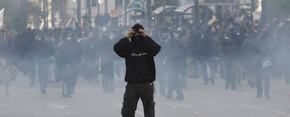 Un joven se cubre en medio de una nube de gas lacrimógeno hoy en Atenas