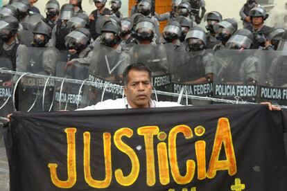 Un manifestante posa con una pancarta pidiendo justicia frente a los policas que bloquean una de las calles de acceso a la plaza principal de Oaxaca.