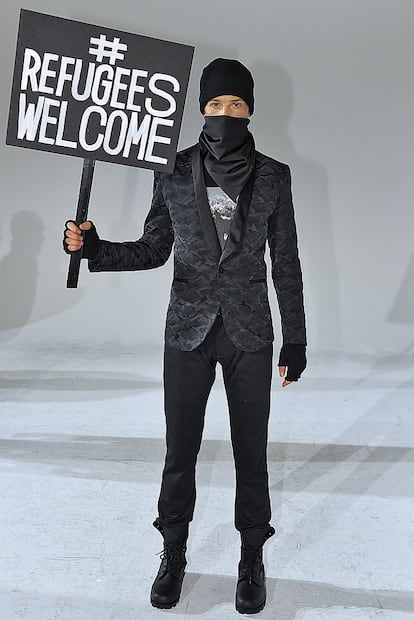 Un modelo posa con un cartel en favor de la llegada de refugiados en la presentación del diseñador Robert James durante la semana de la moda masculina de Nueva York.