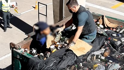 Un agente de la Guardia Civil recata a un migrante entro de un contenedor lleno de fragmentos de vidrio reciclado en el puerto de Melilla.