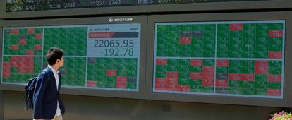 Un peat&oacute;n camina delante de un panel con la evoluci&oacute;n burs&aacute;til de las empresas que cotizan en la Bolsa de Tokio.