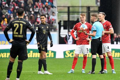 El árbitro Christian Dingert dialoga con sus asistentes por el pinganillo tras detener el encuentro entre el Friburgo y el Bayern.