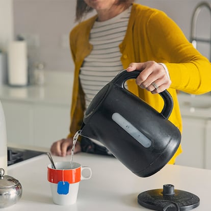 Una mujer echándole agua desde el hervidor a su taza de té.
