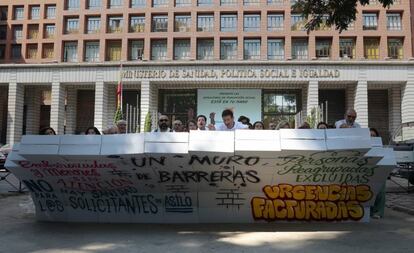 Activistas de varias ONG derriban el muro que simboliza la barrera para el acceso de los inmigrantes a la sanidad universal.