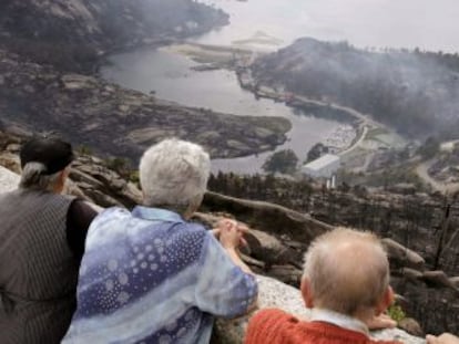 Tres personas observan  los da&ntilde;os del incendio en el monte de &Eacute;zaro (A Coru&ntilde;a).  