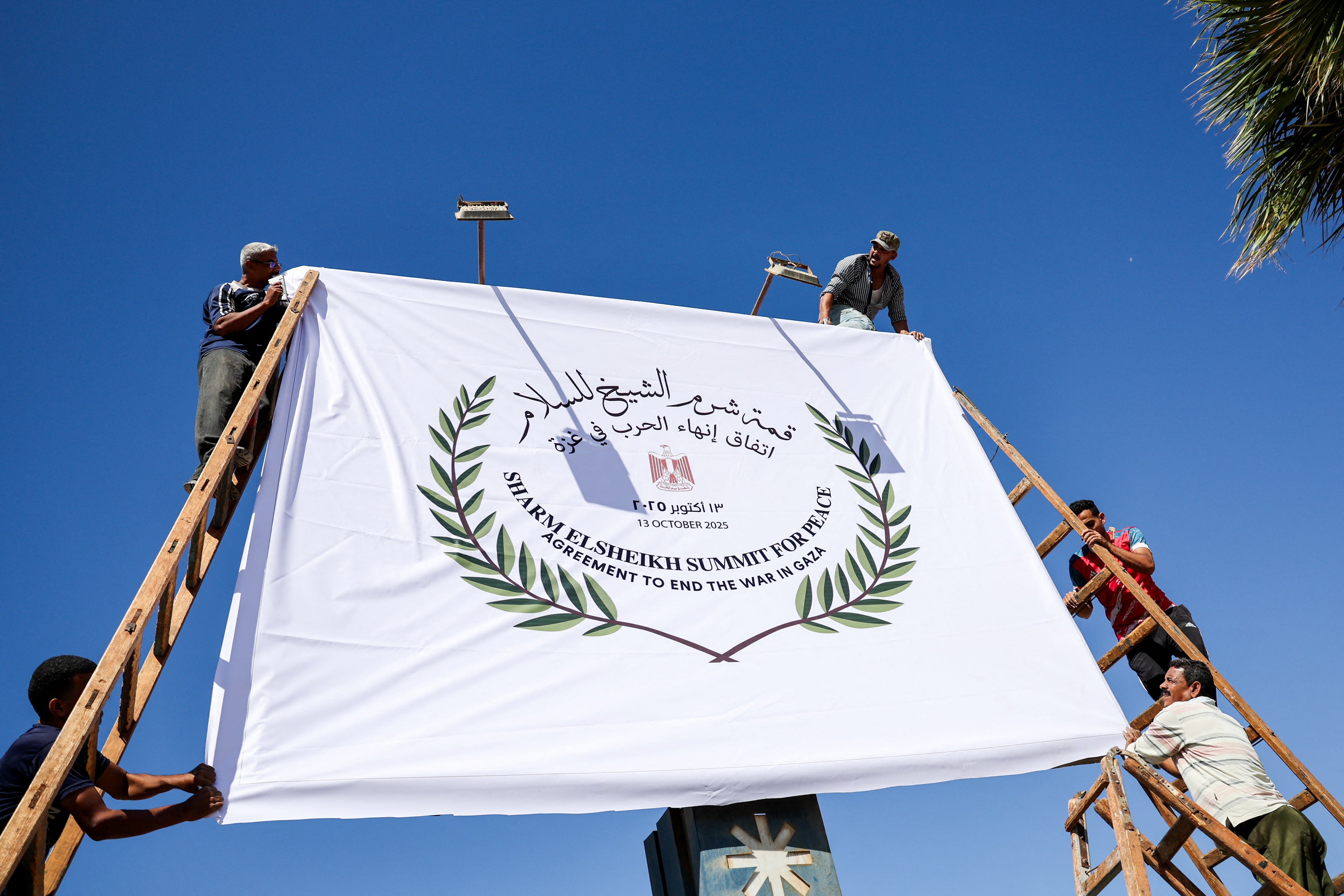 Varios trabajadores cuelgan una pancarta de la cumbre de paz de Sharm el Sheij (Egipto).