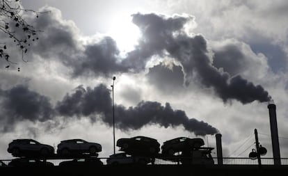 Un camión con coches atraviesa un puente de París ante el humo de una fábrica.