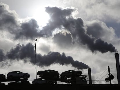 Un camión con coches atraviesa un puente de París ante el humo de una fábrica 