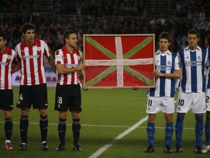 Los futbolistas del Athletic de Bilbao y de la Real Sociedad exhiben una ikurriña durante un derbi.