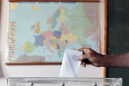 Un hombre deposita su voto en un colegio electoral de Atenas, en el que se ve el mapa de Europa.