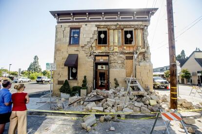 Dos transentes observan la fachada destrozada de un edificio en Napa, donde unos 15 son ahora inhabitables.