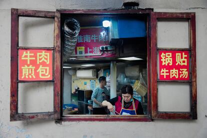 Una mujer vista a través de la ventana cocina en un restaurante callejero, en Pekín, China, 30 de abril de 2024