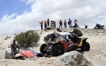 Sainz, sentado en una roca, contempla cómo Lucas Cruz intenta arreglar su Peugeot en la etapa 10ª del Dakar 2016 en La Rioja (Argentina), el 13 de enero de 2016. Sainz rompió la carcasa de la caja de cambios cuando iba primero en la clasificación y tuvo que despedirse de la lucha por el título.