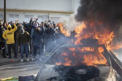 Varios trabajadores protestan junto a un coche ardiendo.