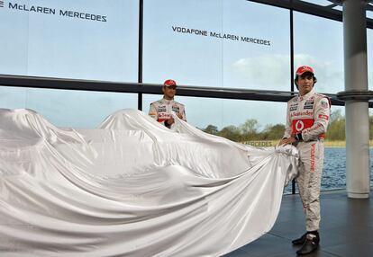 El piloto británico Jenson Button (izquierda) y el mexicano Sergio Pérez,  de McLaren Mercedes, retiran la lona que tapa al nuevo monoplaza de Fórmula Uno de su escudería, el MP4-28, en el centro de tecnología de McLaren en Woking, Reino Unido.
