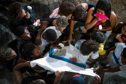 Amigos e familiares de Marcos Vinícios choram sobre sua camiseta da escola manchada de sangue, nesta quinta-feira.