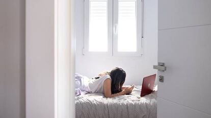 Una joven consulta el móvil y el ordenador en su habitación.