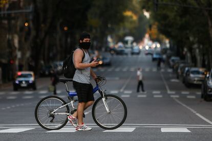 Un hombre que usa un tapabocas cruza la Avenida de Mayo en su bicicleta, este lunes, al cumplirse un mes de la cuarentena obligatoria por el virus COVID-19, en Buenos Aires (Argentina).