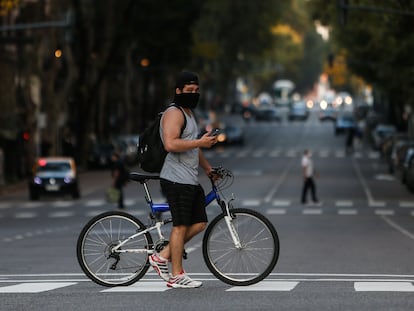 Un hombre que usa un tapabocas cruza la Avenida de Mayo en su bicicleta, este lunes, al cumplirse un mes de la cuarentena obligatoria por el virus COVID-19, en Buenos Aires (Argentina).