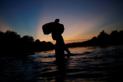 Un migrante que busca refugio en EE UU regresa al lado mexicano con sus pertenencias dentro de una bolsa de plástico mientras cruza el río Bravo para evitar ser deportado.