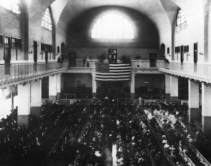 Los inmigrantes esperan sentados en bancos en el halll del edificio de inmigración de Ellis Island, 1903.