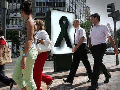 Varios ciudadanos pasan delante de un panel con un crespón negro en una calle de Valencia.