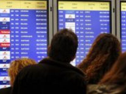 Varias personas consultan en un panel informativo el estado de sus vuelos, en la T-4 del aeropuerto Adolfo Su&aacute;rez Madrid-Barajas.