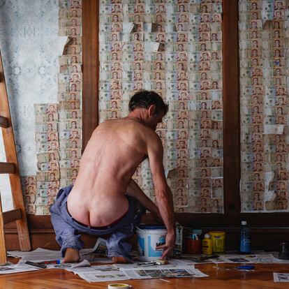 Desnudos frente a la inflación.
Hoy en día, en Argentina valen más las monedas por el metal que como medio de pago y es más barato decorar una pared con billetes de diez pesos, los de menor circulación (inferiores a siete céntimos de dólar), que con vinilo. “Cinco metros con billetes cuestan 5.100 pesos, frente a los 6.500 pesos que cuesta la misma superficie en vinilo”, señala la fotógrafa. El hombre que empapela la habitación es su marido y lleva el pantalón caído para mostrar que la inflación deja desnudos a los argentinos.