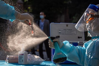 Trabajadores médicos desinfectan un frasco que contiene una muestra de hisopo mientras realizan pruebas de coronavirus, en Pekín (China).