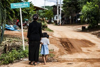 Ranong Kongsaen cogida de la mano de su nieta en la entrada de Na Nong Bong. El letrero al fondo dice: "Cerrad la mina. Rehabilitad. Este pueblo no quiere la mina". Las mujeres del grupo Khon Rak Ban Kerd recibieron un premio de la Comisión Nacional de Derechos Humanos por su defensa de los derechos humanos en el Día Internacional de la Mujer, el 8 de marzo de 2016. "Sigo luchando por las generaciones futuras", remacha Ranong. "No quiero que las próximas generaciones pregunten por qué esta generación no hizo nada para [...] cambiar las cosas. Si tengo que morir por [...] luchar duro contra la injusticia, merece la pena morir de esa manera".