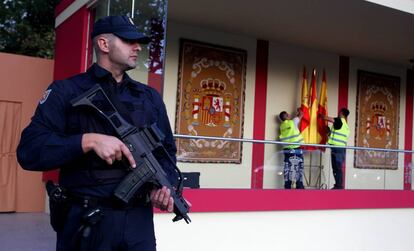 Un policia vigila la tribuna del desfile de la Fiesta Nacional mientras dos operarios ultiman los preparativos.