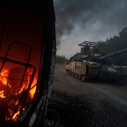 A Ukrainian tank with anti-drone protection passes by a burned-out vehicle in Sumi