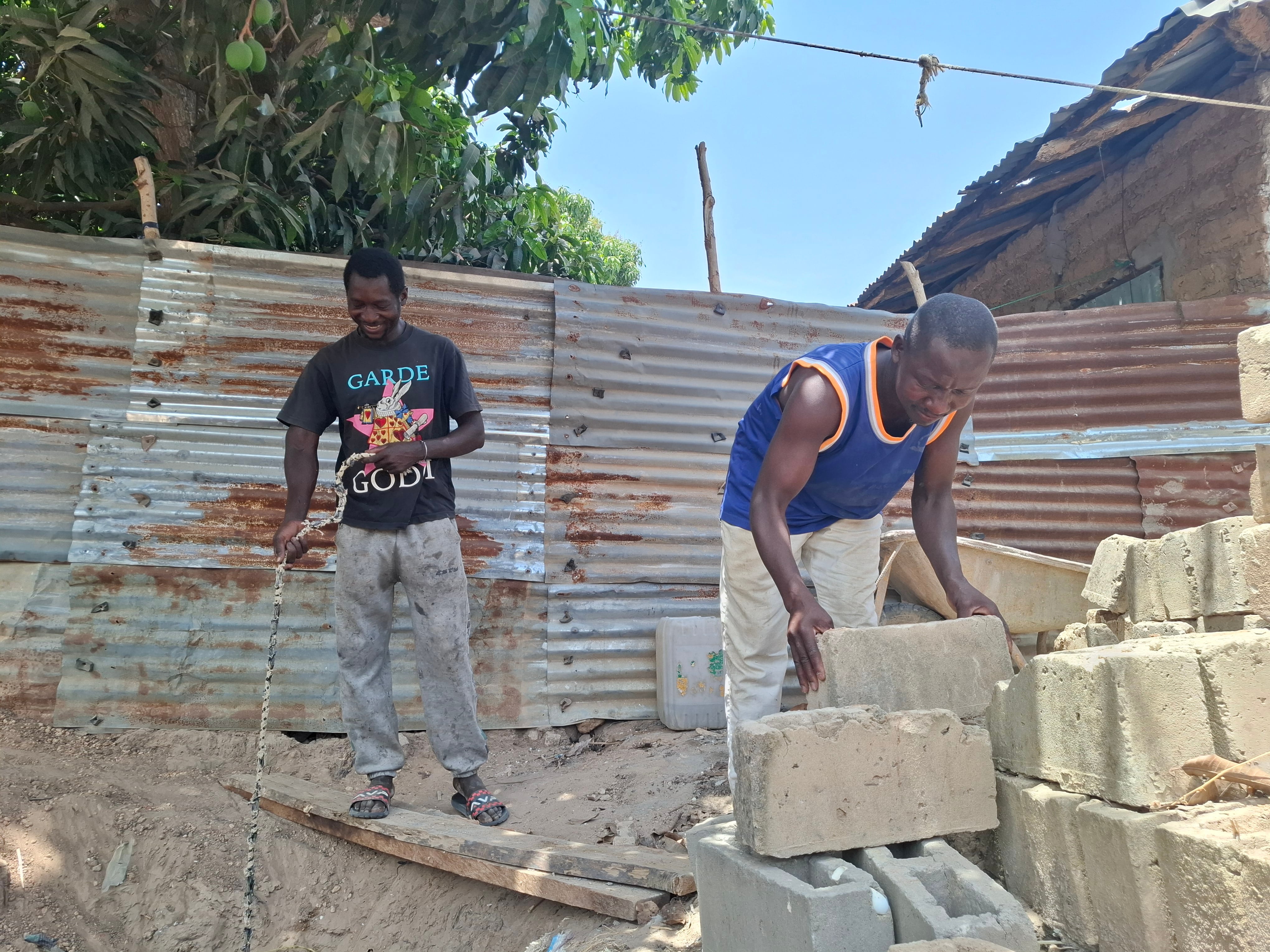 Mohamed Drame (a la derecha) y Salihou, hermanos de Lamine Dramé, desaparecido en 2023, construyen una fosa séptica en su casa de Gunjur (Gambia).