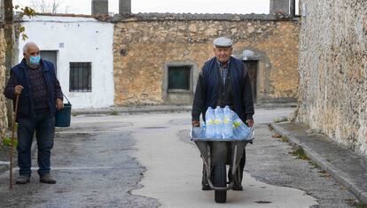 Hermenegildo Cabrero transporta agua embotellada el pasado jueves en Lastras de Cuéllar.  A la izquierda, Pablo Villagrán, el último pastor del pueblo.