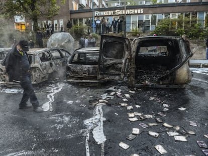 Un hombre camina junto a una hilera de coches carbonizados tras
 los disturbios del jueves, en un suburbio de Estocolmo. 