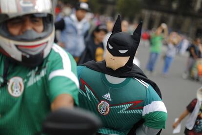 Un aficionado mexicano con un muñeco disfrazado de Batman y un jersey de la selección mexicana.