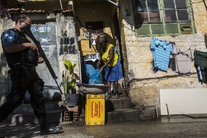 Un policía armado patrulla por la favela Providencia mientras una señora cocina en la puerta de su casa.